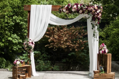 Flowers on a wedding alter that is draped with white fabric with a wall of green plants in the background