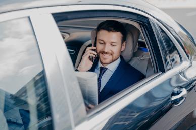 Man sitting in a limousine on a phone call, holding a newspaper with the window down