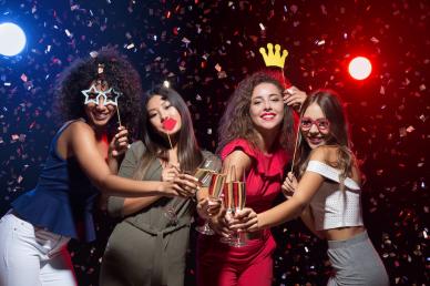 Four woman in a Photo Booth holding champagne glasses and party accessories