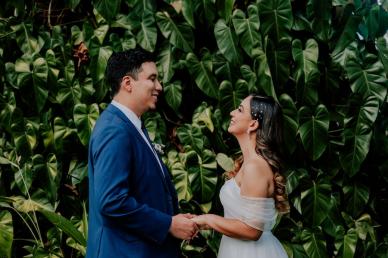 Bride and groom holding hands in front of a green plant wall at their wedding