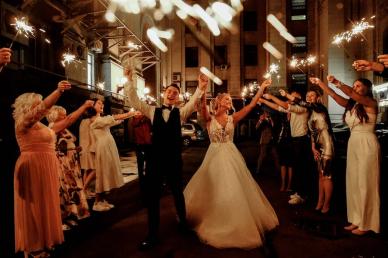 Bride and groom leaving their wedding at night with guests holding sparklers