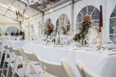 Table with white table cloth and white chairs within a large tent for a wedding reception