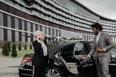 Woman in a suit, on the phone, with a chauffeur opening the door of the limo for her