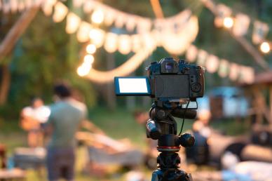 Video camera set up to film an event with stringing lights above the party
