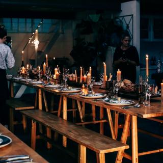 Wooden table with place settings and crew setting up the venue, ladder in frame