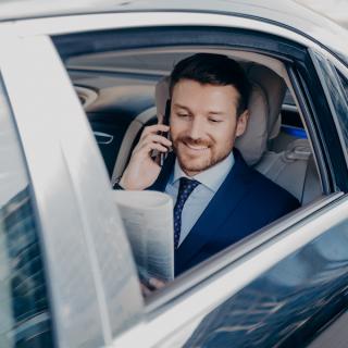 Man sitting in a limousine on a phone call, holding a newspaper with the window down