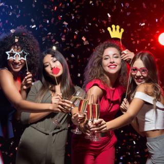 Four woman in a Photo Booth holding champagne glasses and party accessories