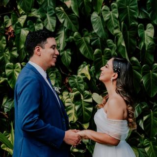 Bride and groom holding hands in front of a green plant wall at their wedding