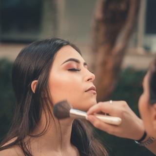 Makeup artist applying bronzer with a brush to a client with dark brown hair