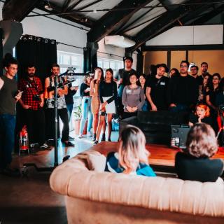 Corporate event taking place with people standing around and others sitting on a couch, with videographers filming