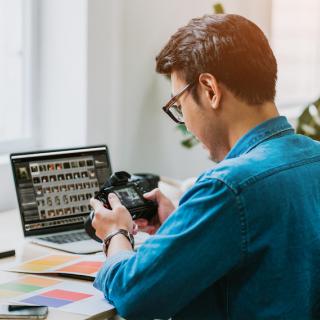 photographer looking at the screen on his professional camera, with his computer monitor in the background